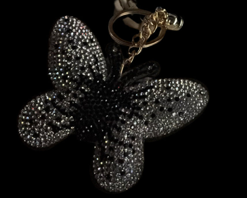 Beige handbag with a decorative black flower charm on a dark background